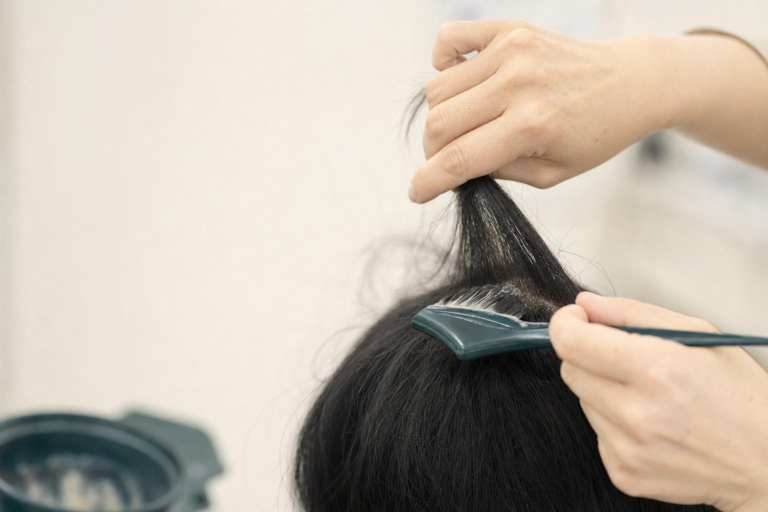 髪の一房を指ではさみ、刷毛で根元に薬剤を塗っている手元