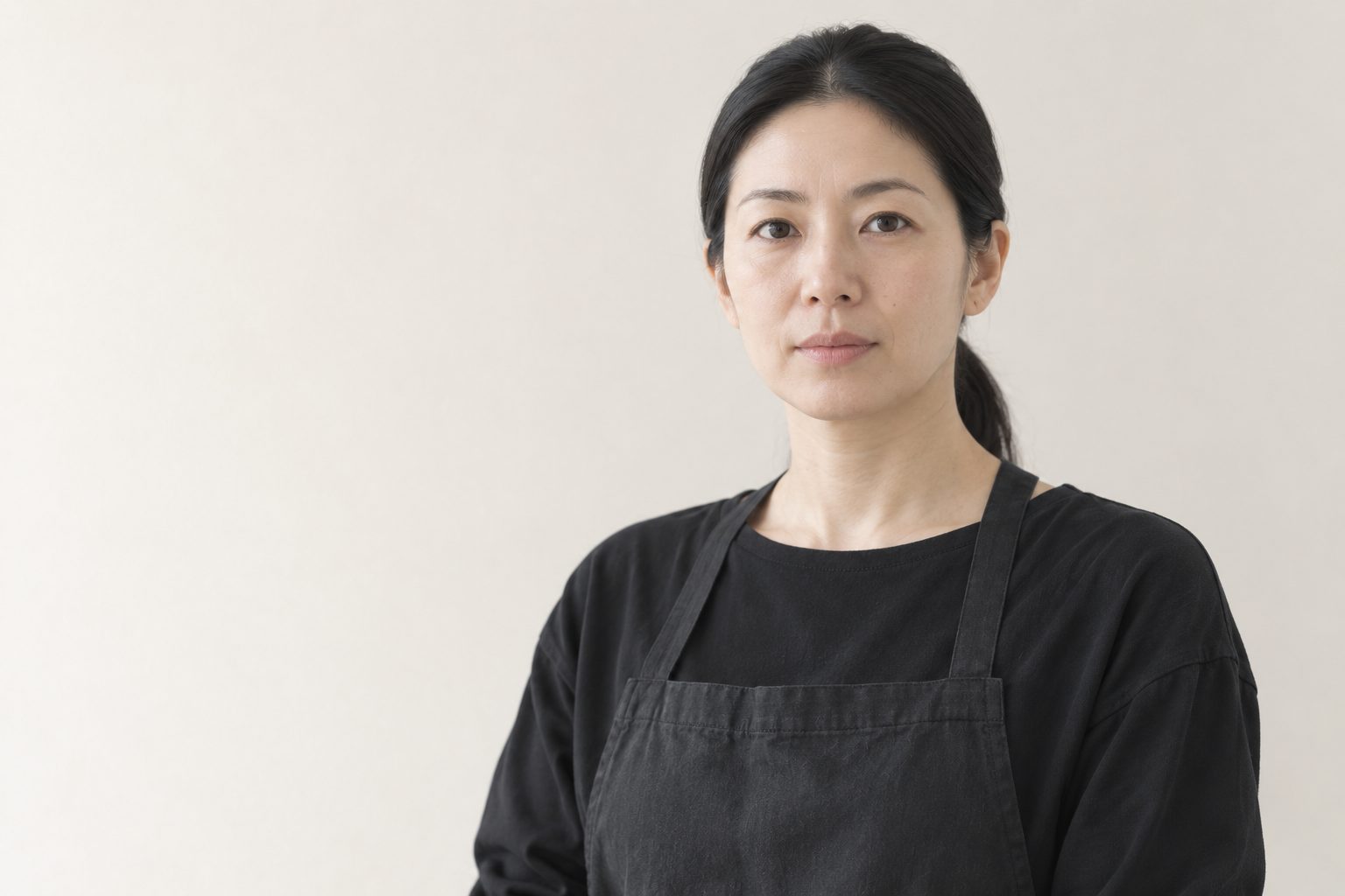 nagi（凪）の施術者・白石奈津。黒の無地の服とエプロン姿で、静かにカメラを見ている